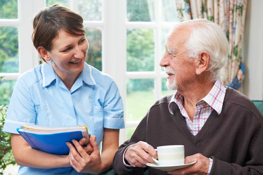 Caregiver helps an older resident walk safely through a bright assisted living hallway.